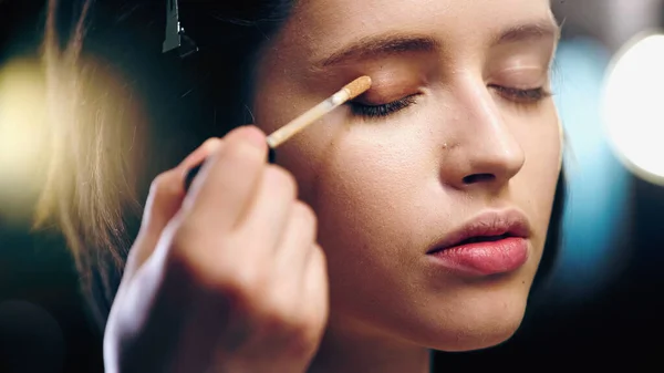 Makeup artist applying concealer on eyelid of young woman — Stock Photo