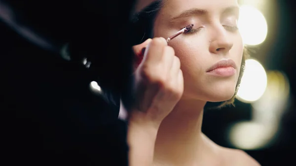 Blurred makeup artist applying liquid eye shadow on eyelid of model — Stock Photo