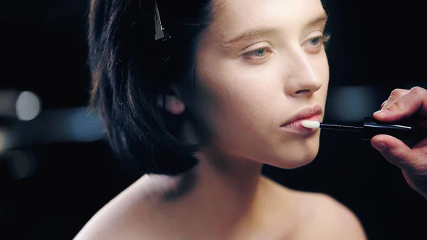 Artista de maquiagem aplicando brilho labial em lábios de modelo com ombros nus — Fotografia de Stock