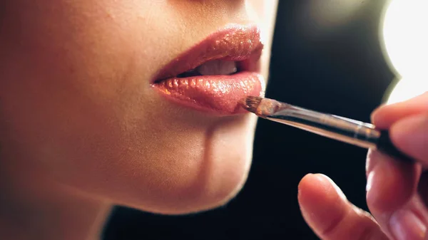 Cropped view of makeup artist applying lip gloss on lips of model — Stock Photo