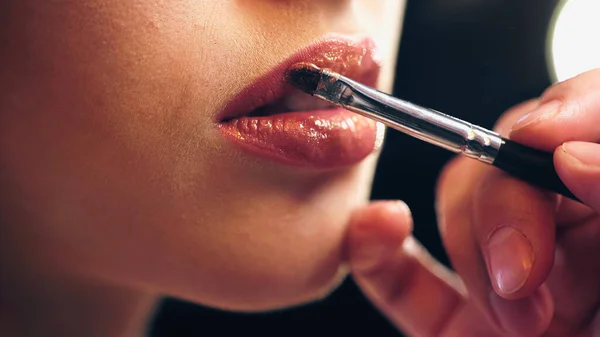 Recortado vista de artista de maquillaje aplicando brillo de labios en los labios de la mujer - foto de stock