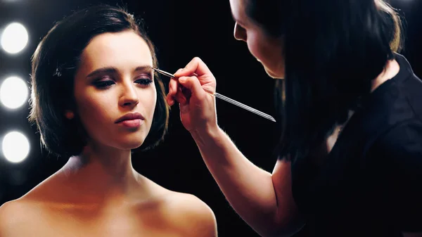 Makeup artist styling eyebrows of young woman with bare shoulders — Stock Photo