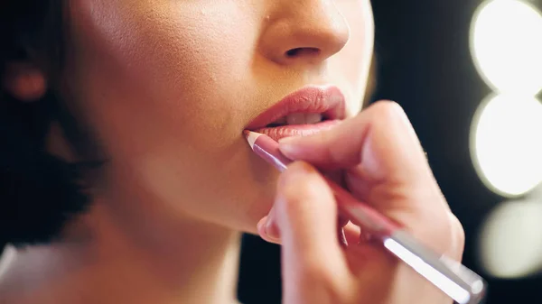 Vista cortada de artista de maquiagem borrada aplicando lápis de lábio em lábios de mulher — Fotografia de Stock