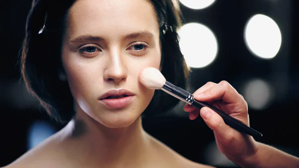 Maquilleur appliquer fond de teint visage avec pinceau cosmétique sur la peau de brunette jeune modèle — Photo de stock