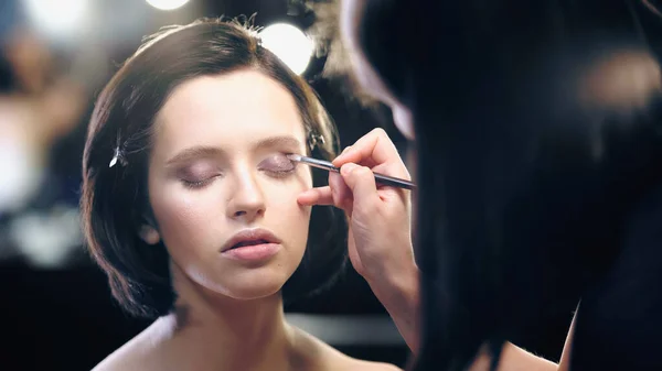 Makeup artist applying eye shadow with cosmetic brush on young pretty model with closed eyes — Stock Photo