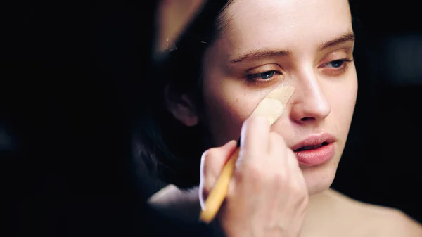 Makeup artist holding cosmetic brush while applying makeup foundation on face of model — Stock Photo