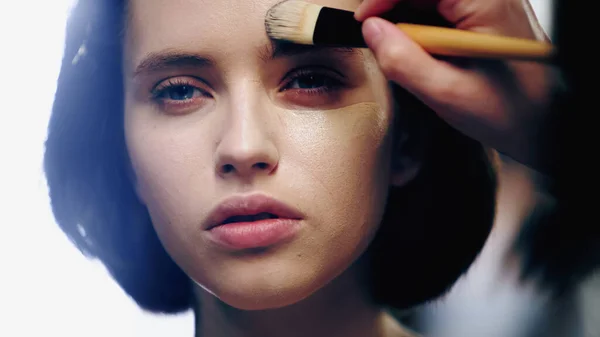 Maquillaje artista celebración de cepillo cosmético mientras se aplica la base de la cara en el modelo centrado - foto de stock