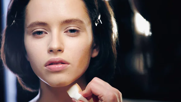 Make-up-Artist hält Kosmetikschwamm beim Auftragen von Gesichtsfundament auf Modell — Stockfoto
