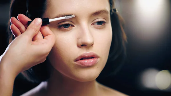 Makeup artist brushing eyebrow of young model — Stock Photo