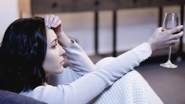 Verärgerte Frau in Decke gehüllt sitzt mit Glas Wein auf Sofa und hält daheim die Hand vor dem Gesicht — Stockfoto