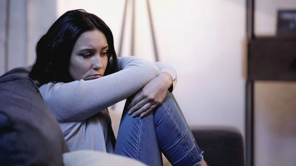 Depressed woman sitting on sofa in self hug pose at home — Stock Photo