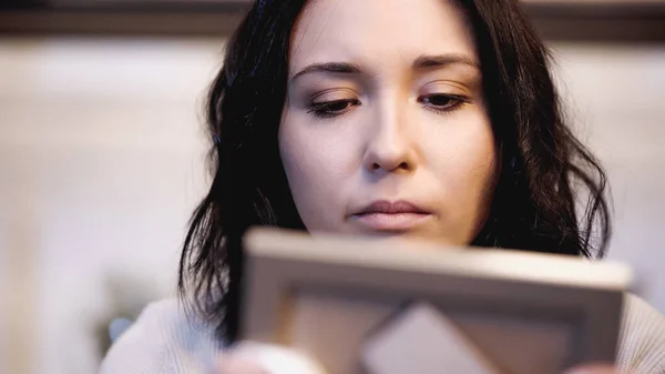 Close up view of upset woman looking at photo frame photo frame at home — Stock Photo