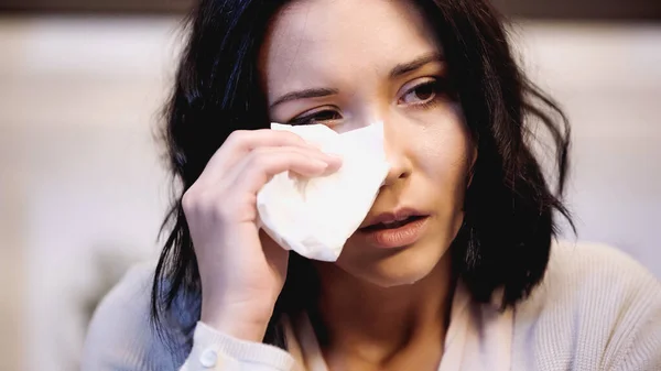Portrait of crying brunette woman wiping tears with white paper napkin at home — Stock Photo