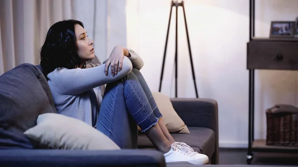 Upset woman sitting on sofa in self hug pose at home — Stock Photo