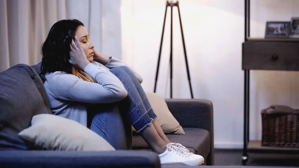 Расстроенная женщина сидит на диване и держит руки возле лица дома — стоковое фото