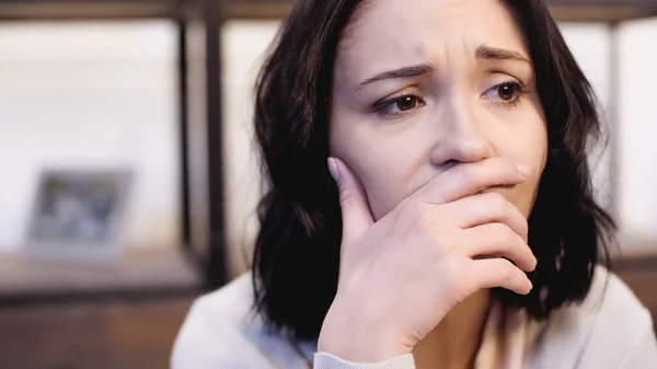 Porträt einer depressiven brünetten Frau im beigen Pullover, die zu Hause den Mund mit der Hand bedeckt — Stockfoto