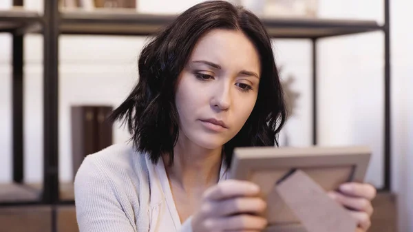 Upset brunette woman looking at blurred photo frame in hands at home — Stock Photo