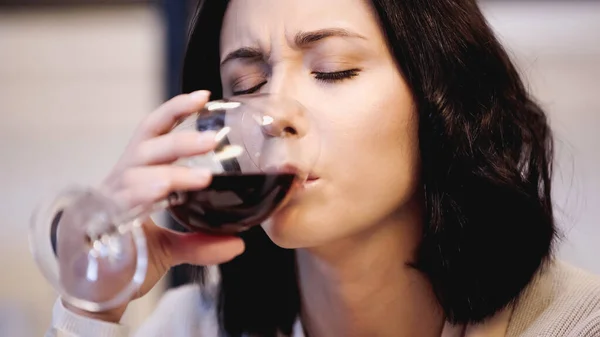 Close up view of upset woman drinking red wine from glass with closed eyes at home — Stock Photo
