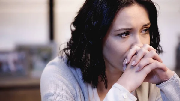 Upset woman sitting and covering mouth with clenched hands at home — Stock Photo