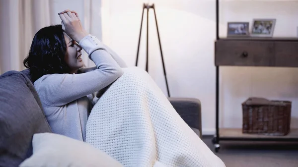 Женщина плачет на диване и покрывает лицо руками дома — стоковое фото