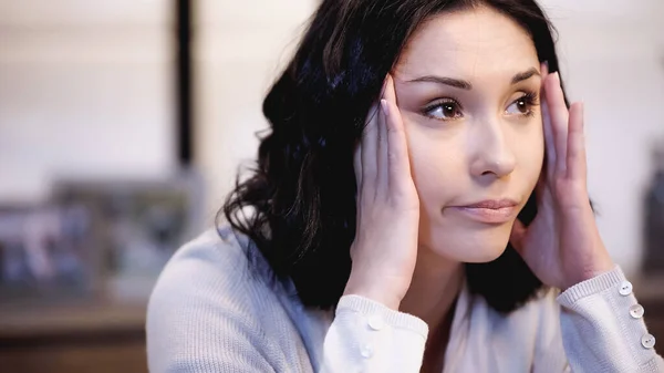 Depressed woman with migraine holding hands near head at home — Stock Photo