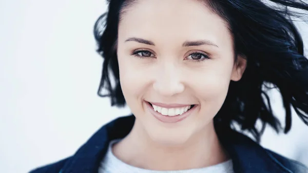 Lächeln brünette Frau mit Haaren auf Wind auf grauem Hintergrund — Stockfoto