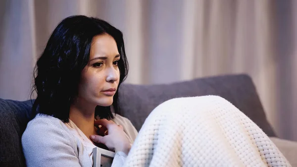 Depressed woman covered in blanket sitting on sofa and hugging photo frame at home — Stock Photo