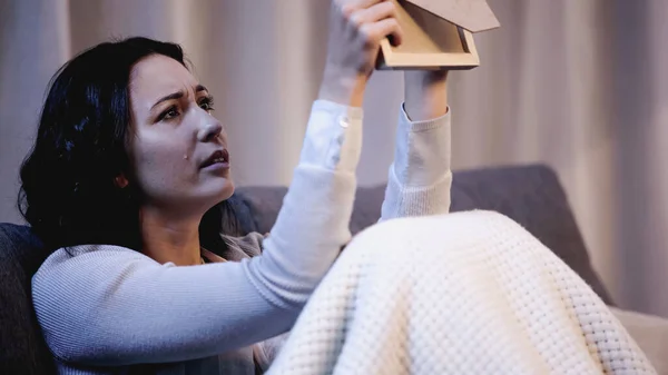 Upset woman sitting on sofa, holding photo frame and crying at home — Stock Photo