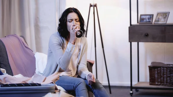 Depressed woman sitting on sofa near male clothes and drinking red wine from glass at home — Stock Photo