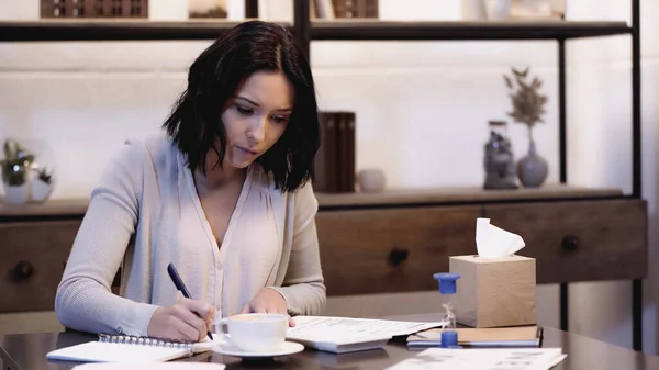 Концентрированная женщина сидит на столе и делает бумажную работу дома — стоковое фото