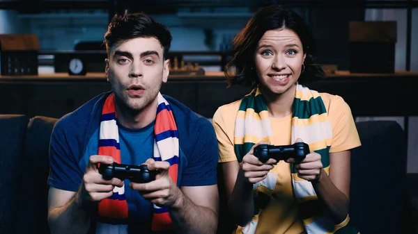 KYIV, UKRAINE - JUNE 09, 2021: tensed couple in striped scarfs holding joysticks and playing video game — Stock Photo