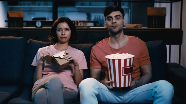 Homme tenant seau avec pop-corn et regarder le film avec petite amie tenant boîte en carton avec de la nourriture chinoise — Photo de stock