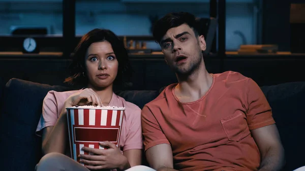 Mujer sorprendida sosteniendo palomitas de maíz cubo y viendo la película con el novio - foto de stock