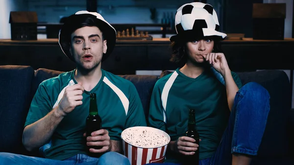 Fãs de futebol estressado em chapéus de fãs segurando garrafas de cerveja e assistindo campeonato na sala de estar — Fotografia de Stock