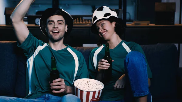 Fans de football heureux dans des chapeaux de ventilateur tenant des bouteilles de bière et se réjouissant tout en regardant le championnat — Photo de stock