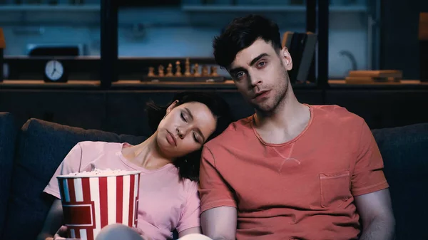 Tired woman with popcorn bucket sleeping on shoulder of boyfriend in living room — Stock Photo