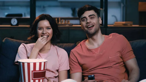 Happy woman eating popcorn and watching comedy movie with cheerful boyfriend — Stock Photo