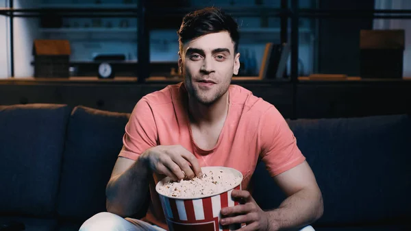 Mann hält Popcorn-Eimer in der Hand und schaut sich Film zu Hause an — Stockfoto
