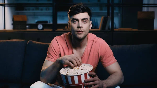 Hombre sosteniendo palomitas de maíz cubo y viendo la película en casa - foto de stock