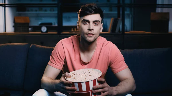 Gutaussehender Mann hält Popcorn-Eimer, während er sich zu Hause einen Film ansieht — Stockfoto