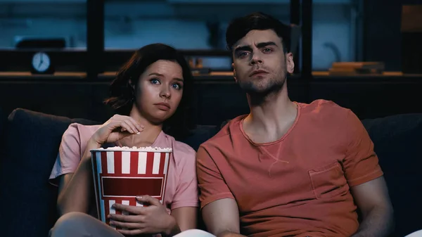 Напряженная женщина держит ведро попкорна и смотрит кино с парнем — стоковое фото