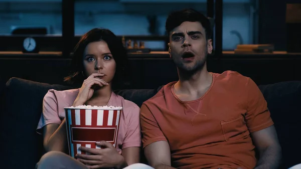 Mujer asustada sosteniendo palomitas de maíz cubo y viendo película con novio - foto de stock