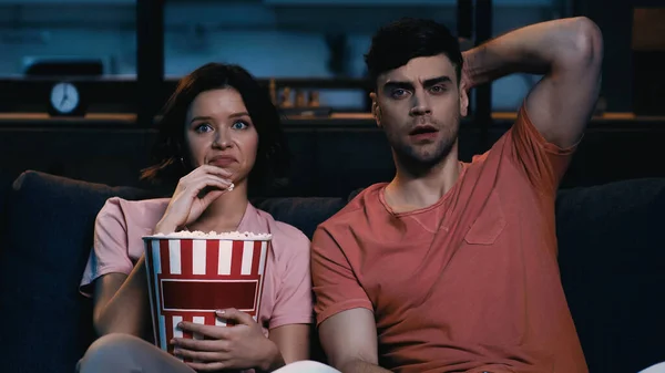 Mulher enojada segurando balde de pipoca e assistindo filme com namorado chocado — Fotografia de Stock