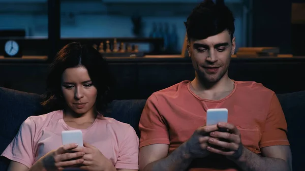 Mann und Frau SMS auf Mobiltelefonen im modernen Wohnzimmer — Stockfoto