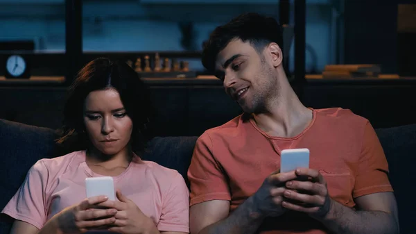 Glücklicher Mann schaut Frau beim SMS-Schreiben auf Handy im modernen Wohnzimmer an — Stockfoto