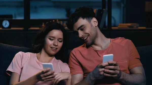 Sorridente homem e mulher olhando para o celular na sala de estar moderna — Fotografia de Stock