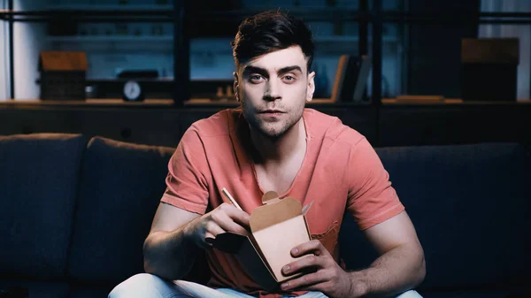 Man holding cardboard box with chinese food and watching movie at home — Stock Photo