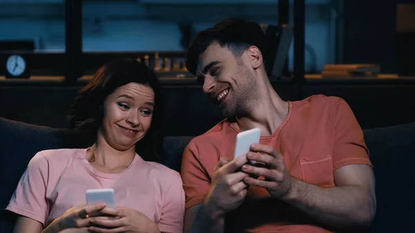 Fröhliche Männer und Frauen, die im modernen Wohnzimmer auf ihr Smartphone schauen und lächeln — Stockfoto