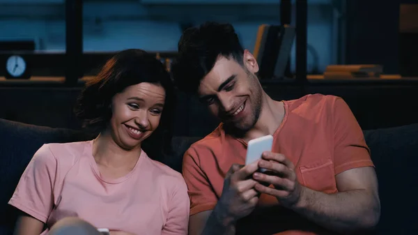 Fröhliche Männer und Frauen, die im modernen Wohnzimmer auf ihr Smartphone schauen und lächeln — Stockfoto