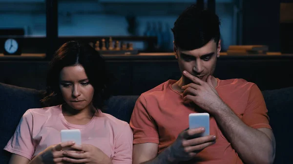 Nachdenkliche Männer- und Frauennachrichten auf Mobiltelefonen im modernen Wohnzimmer — Stockfoto